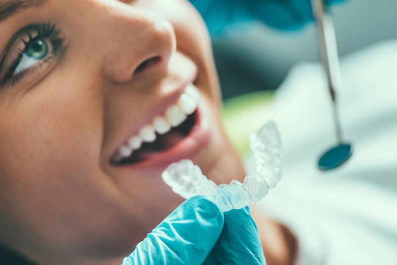 Close up photo of a doctor holding a clear aligner up to a female patient’s teeth